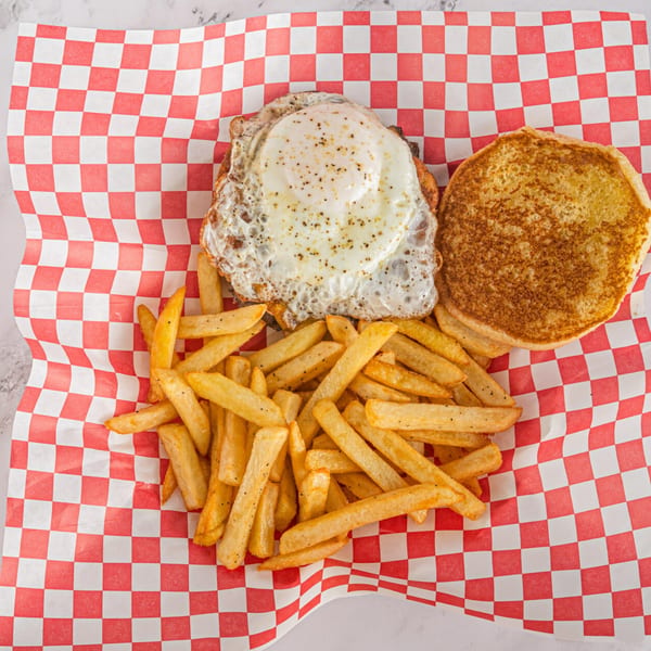Hot Chicken and Breakfast sandwich with a fried egg, open-faced, served with fries on checkered paper.