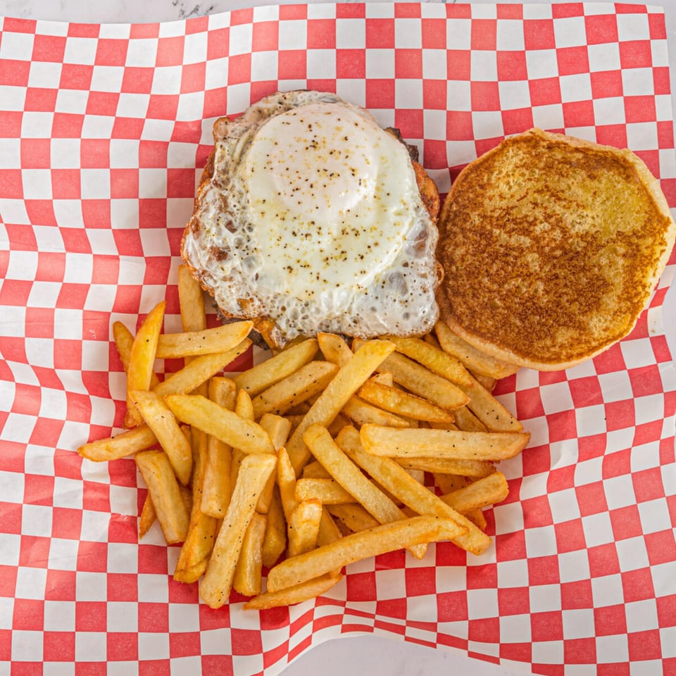 Hot Chicken and Breakfast sandwich with a fried egg and fries on red and white checkered paper.