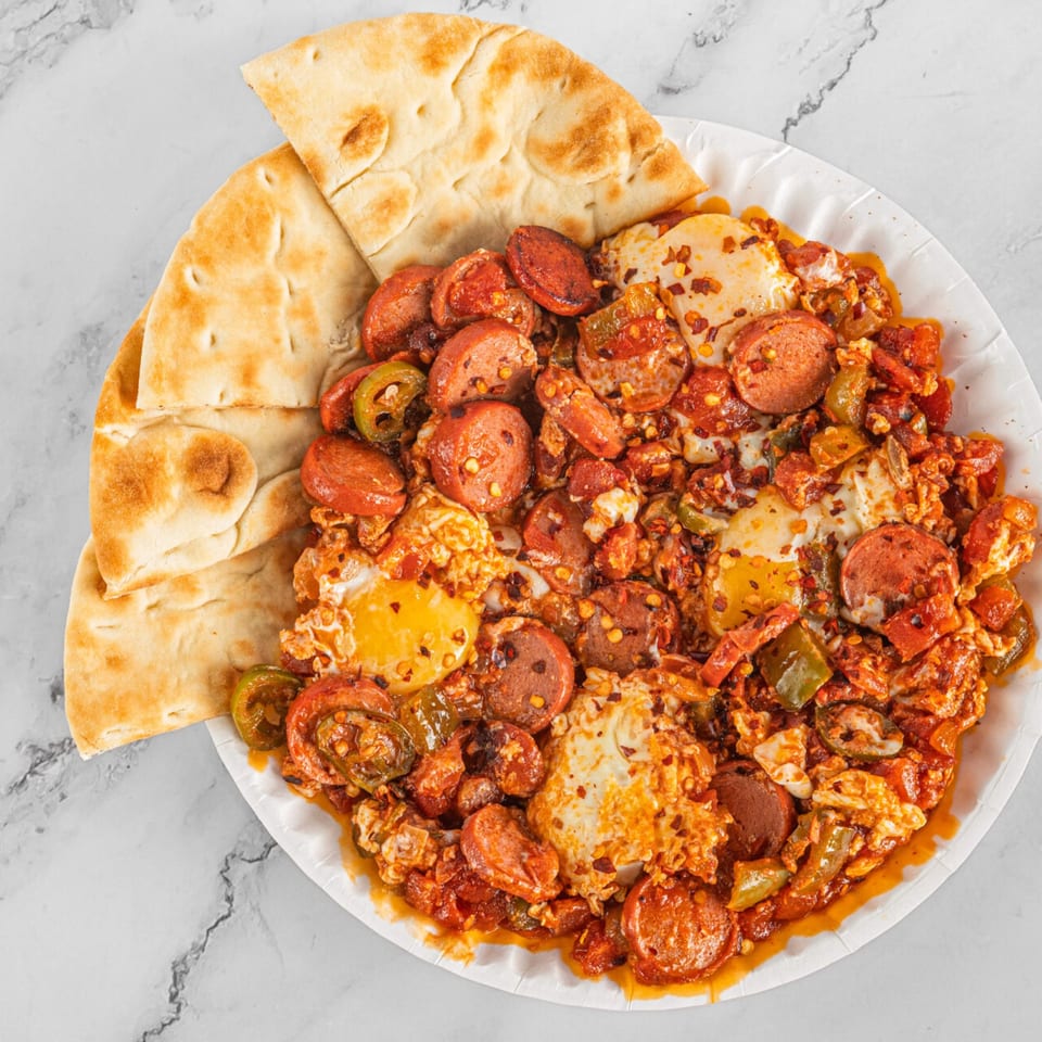 Spicy breakfast skillet with eggs, sausage, peppers, and flatbread on a white plate.