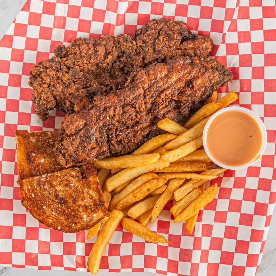 Hot Chicken and Breakfast's fried chicken tenders, fries, Texas toast, and dipping sauce on checkered paper.