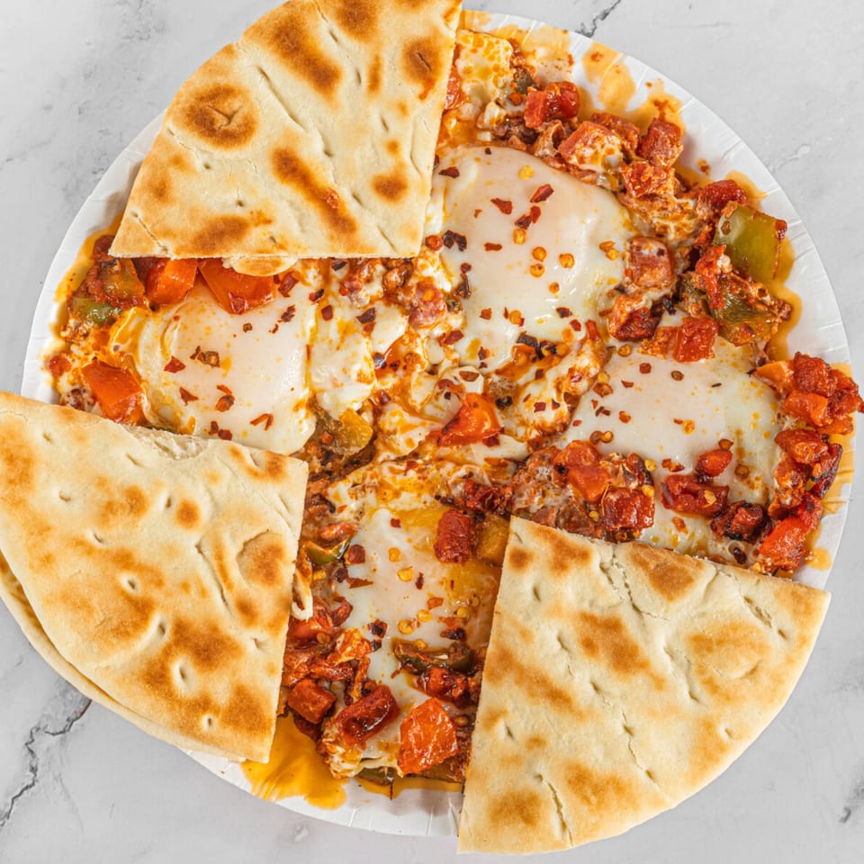 Shakshuka with four pieces of pita bread on a white plate, garnished with chili flakes.
